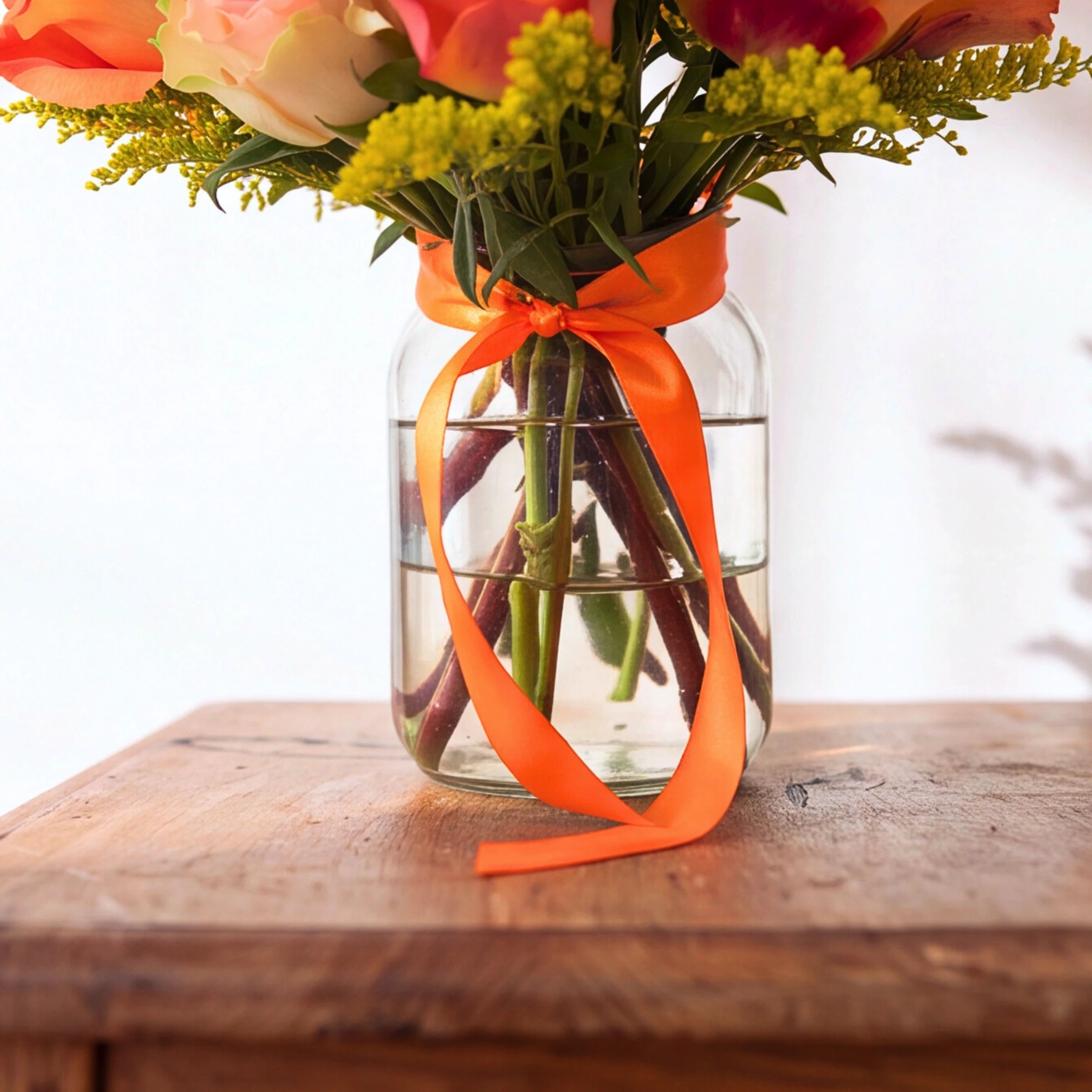Clear glass vase with orange satin ribbon and stems from the Sunlit Gratitude rose arrangement