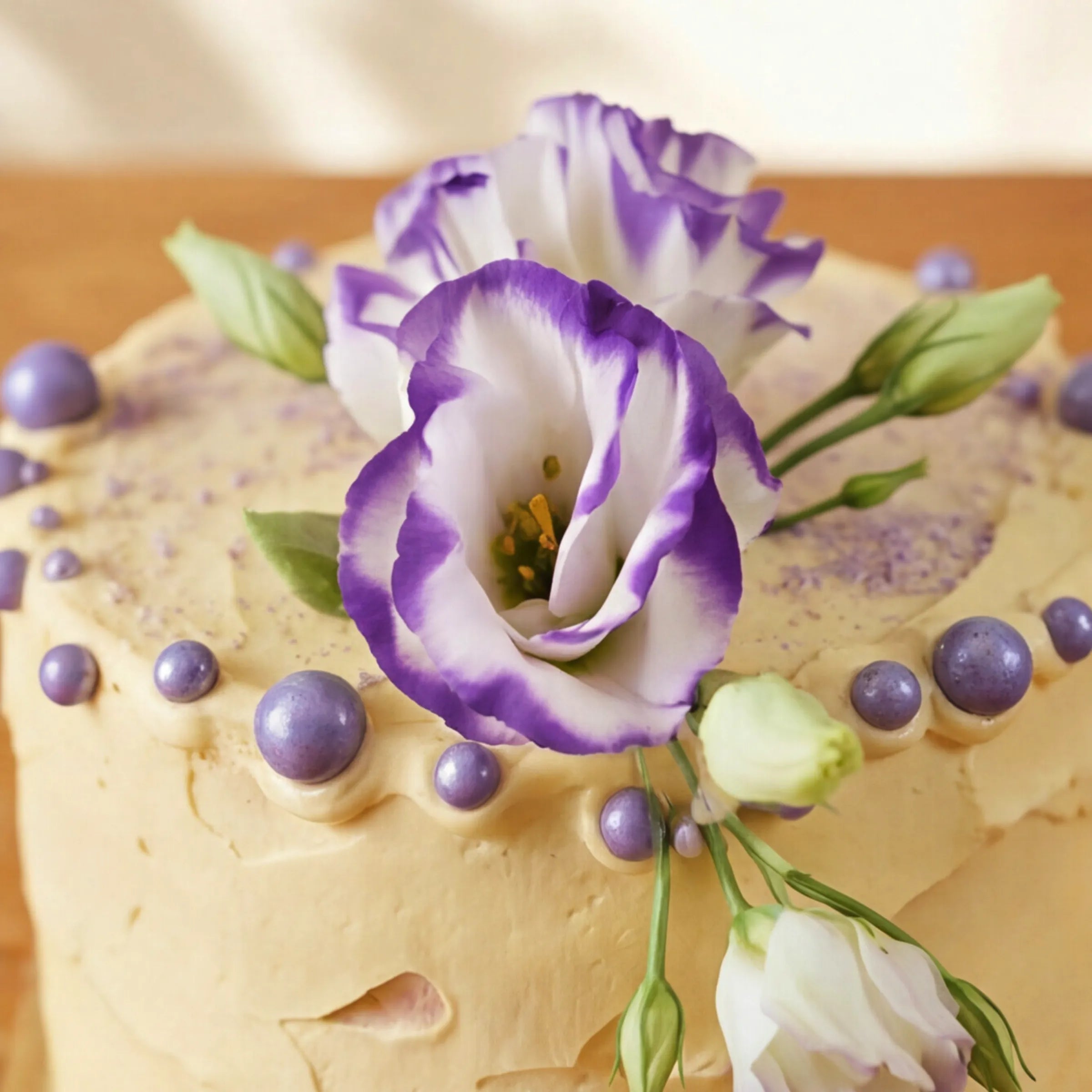 Macro of buttercream cake topped with purple lisianthus and lilac chocolate pearls from Sweet Celebration