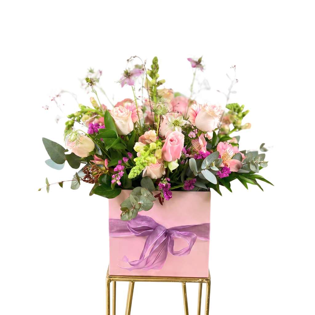 Box arrangement of flowers in a pink box with a purple ribbon on a white background