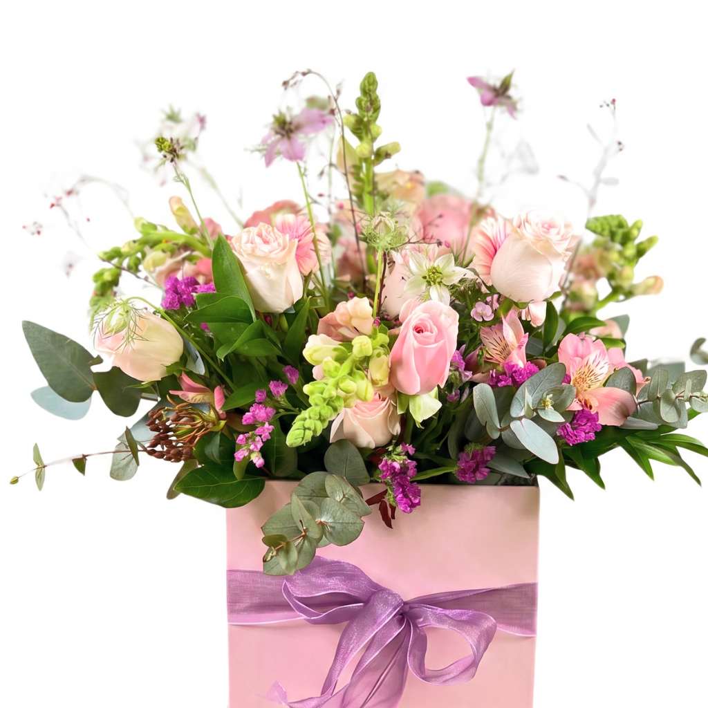 Arrangement of flowers in a pink box with a purple ribbon on a white background