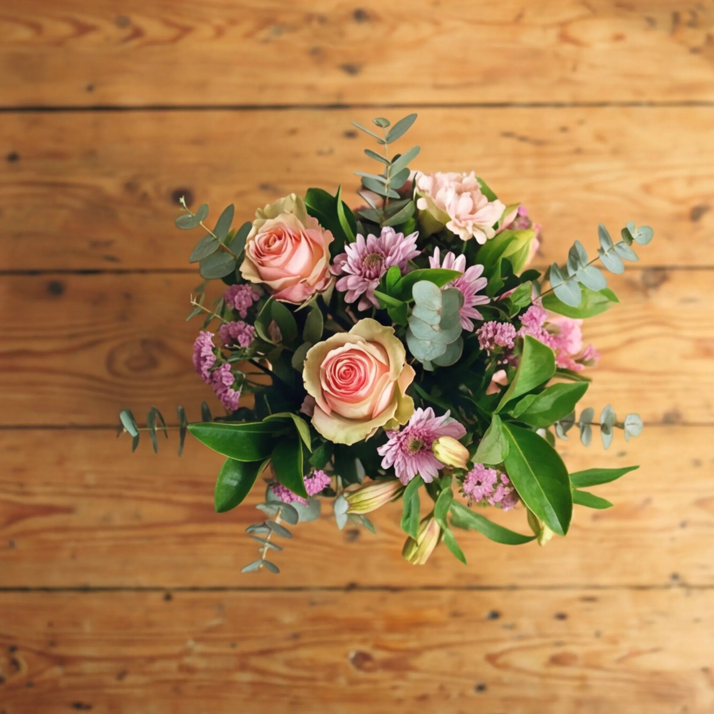 Top view of Sweet Pea in a Jar with peach roses, lilac chrysanthemums, pink statice and silver eucalyptus on a wooden table
