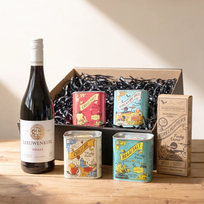 Bottle of Leeuwenkuil Shiraz beside an open gift box with four Funky Ouma spice tins and a box of firelighters on a pine table, Fabulous Flowers South Africa