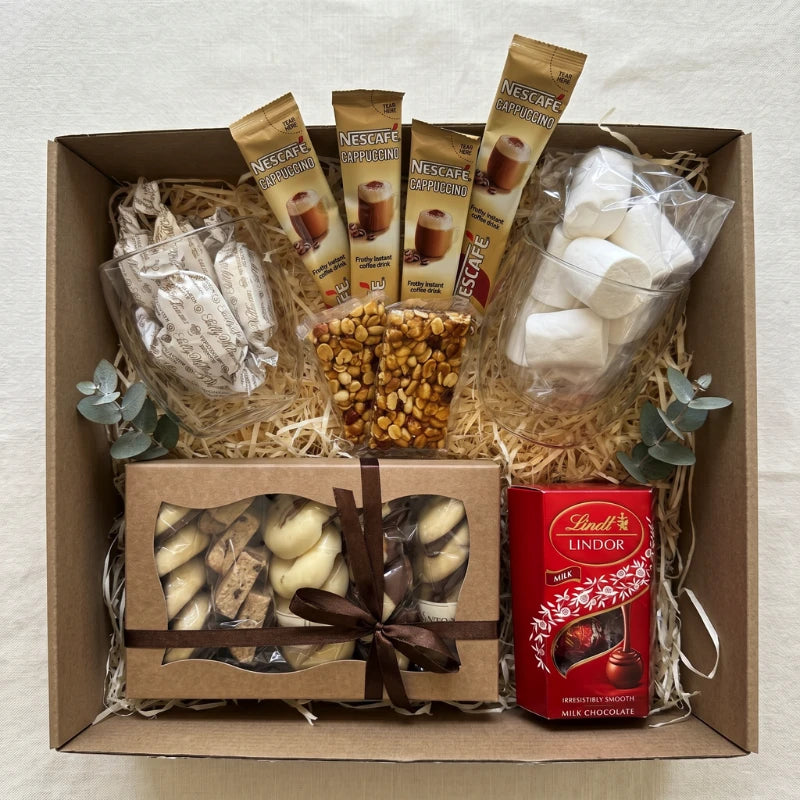 The Coffee Break Box top-down with four Nescafé Cappuccino sachets, Sally Williams nougat in a glass, peanut brittle bars, marshmallows, ribboned florentines and Lindt Lindor milk chocolate, by Fabulous Flowers and Gifts