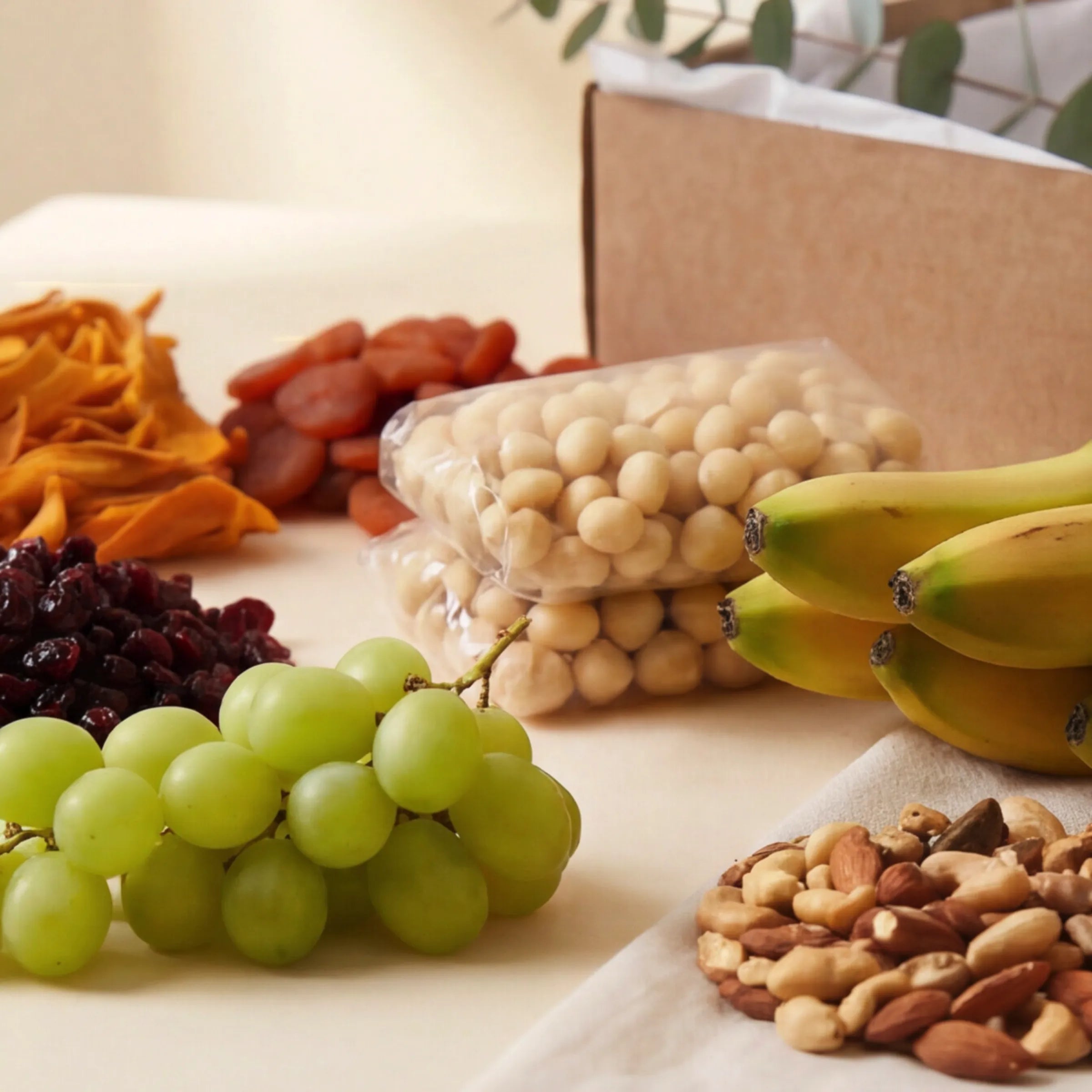 The Healthy Collection from Fabulous Flowers South Africa styled on a linen cloth, a wellness gift box of macadamia nuts, dried mango, apricots, cranberries, mixed nuts, fresh bananas and grapes, ideal as a healthy birthday, get-well or corporate gift