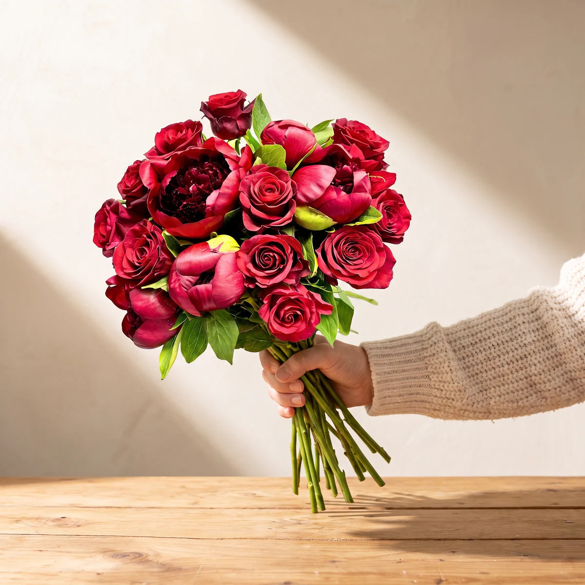 Hand holding out The Bloom Between Us red peony and red rose bouquet