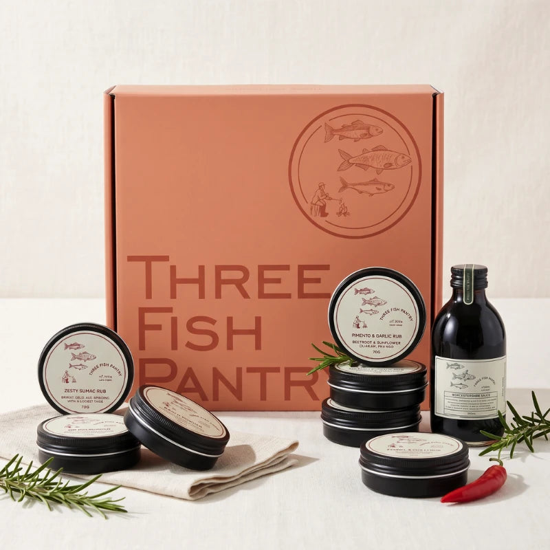 Three Fish Pantry Signature Rubs & Sauce styled with open Pimento & Garlic Rub tin, fresh red chilli, rosemary, wooden spoon, Zesty Sumac and Ranch Powder tins and the Three Fish Pantry Worcestershire Sauce bottle, Fabulous Flowers and Gifts