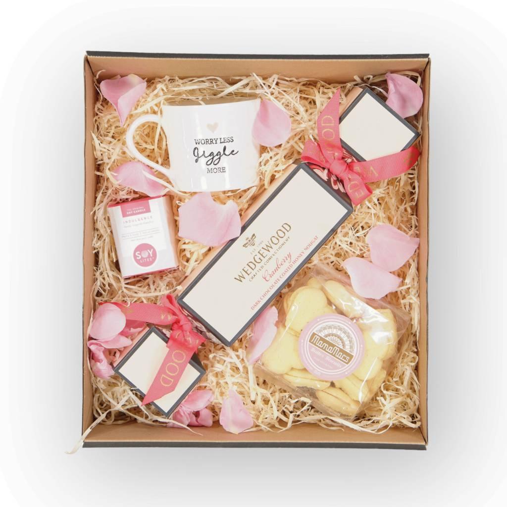Pamper hamper packed with Wedgewood Dark Chocolate & Cranberry Honey Nougat, A Pink and White “Worry Less and Giggle More” Mug, Mini Candle with vanilla, grapefruit and ginger scents, MamaMacs Butter Biscuits - Fabulous Flowers