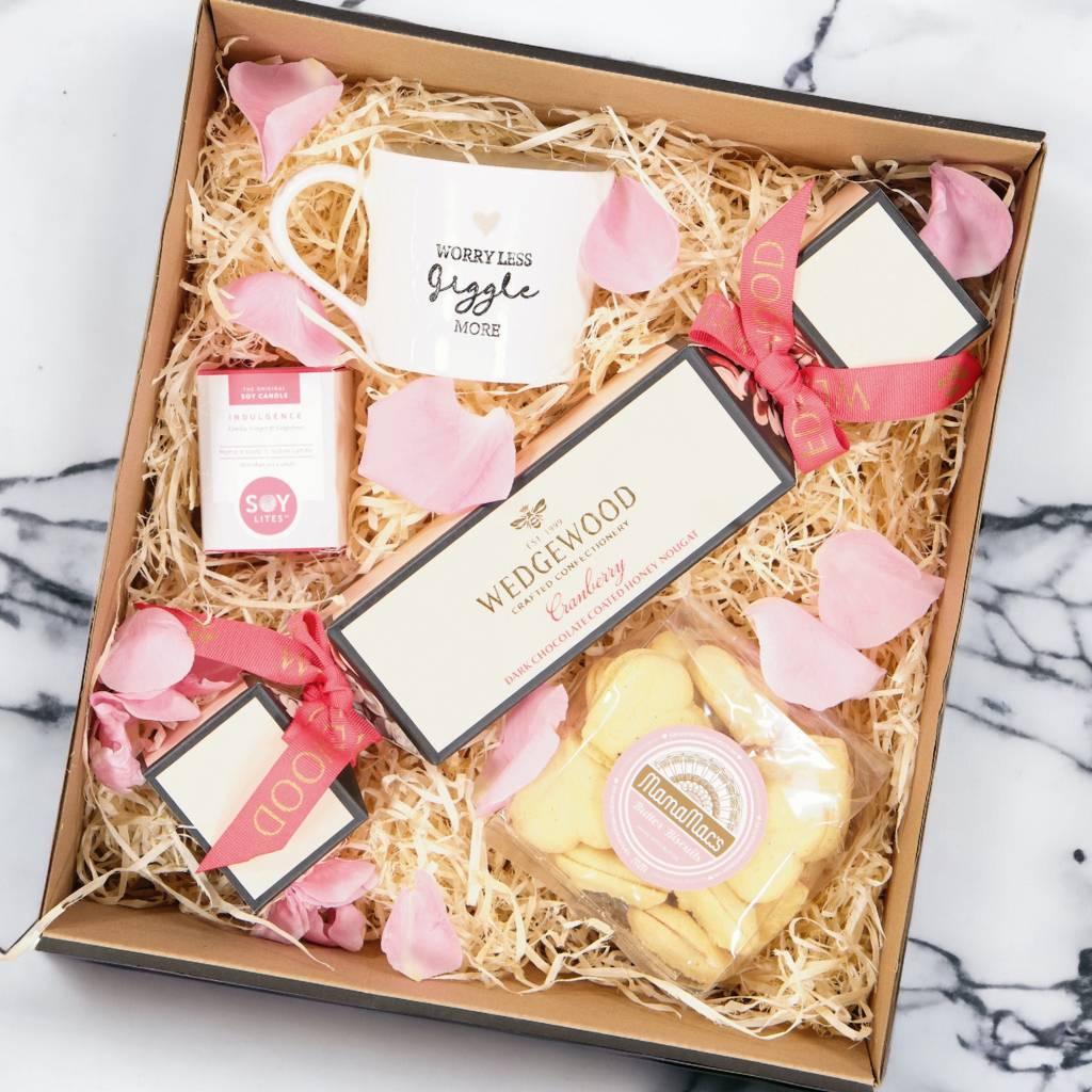 Pamper hamper packed with Wedgewood Dark Chocolate & Cranberry Honey Nougat, A Pink and White “Worry Less and Giggle More” Mug, Mini Candle with vanilla, grapefruit and ginger scents, MamaMacs Butter Biscuits - Fabulous Flowers