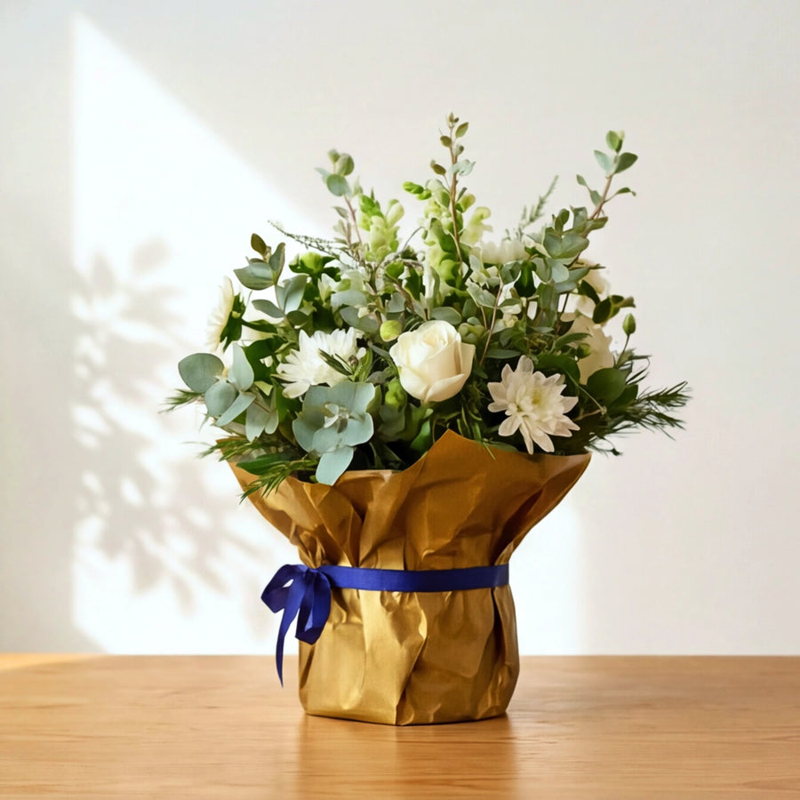 White sympathy flowers with eucalyptus and pine, wrapped in gold paper with a navy blue bow.