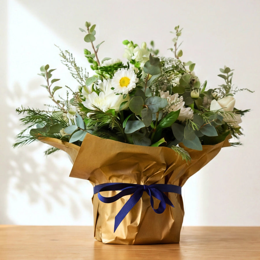 Tranquility white flower arrangement in gold wrap with a navy ribbon, white blooms and eucalyptus.