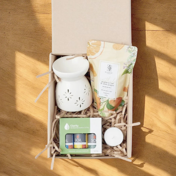 Kraft gift box from above with a white ceramic oil burner, SOiL Clarity essential oil trio, Dinaledi mandarin bath salt and a tealight on a sunlit pine table, Fabulous Flowers South Africa