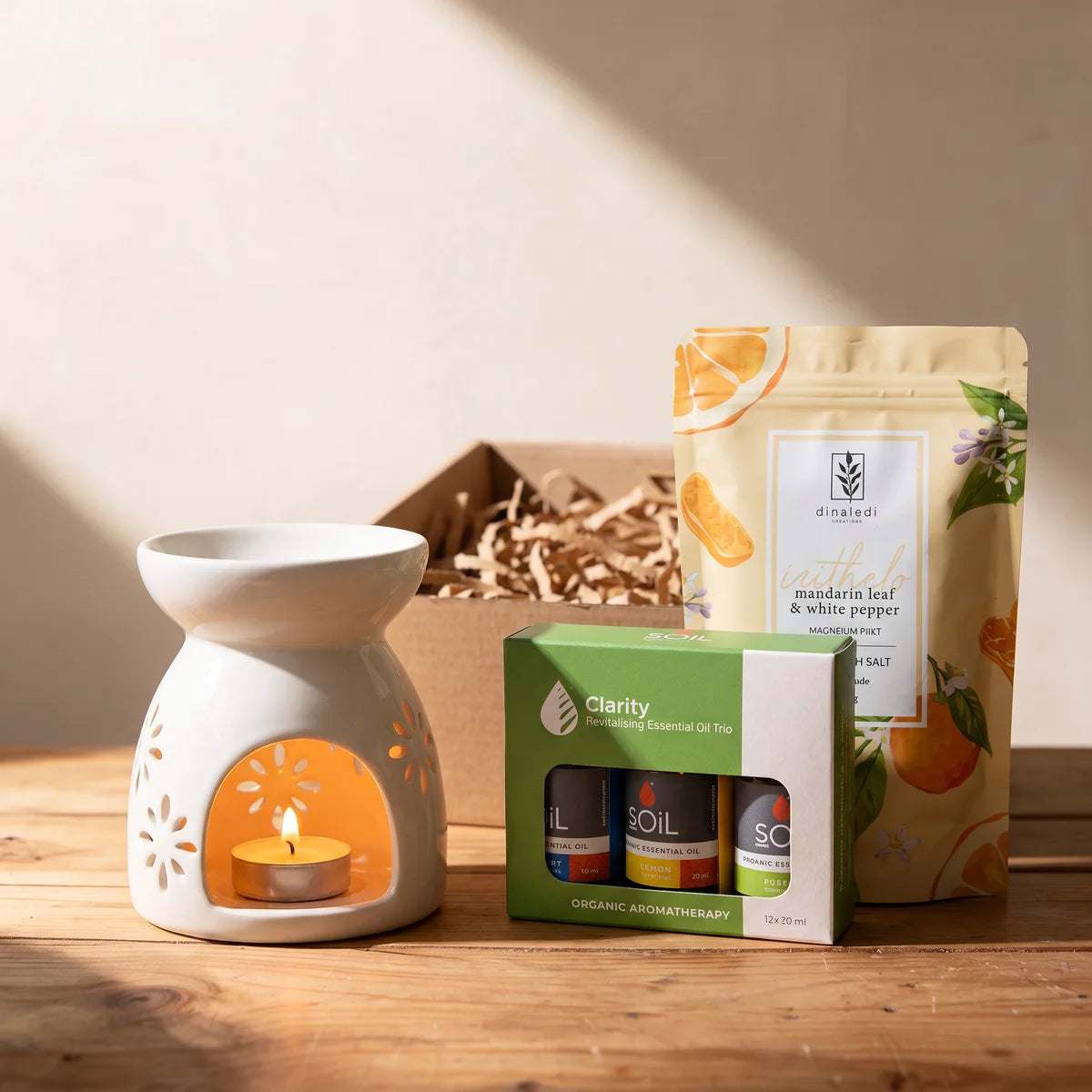 White ceramic oil burner glowing with a lit tea light beside a box of essential oils and a pouch of bath salts, Fabulous Flowers South Africa