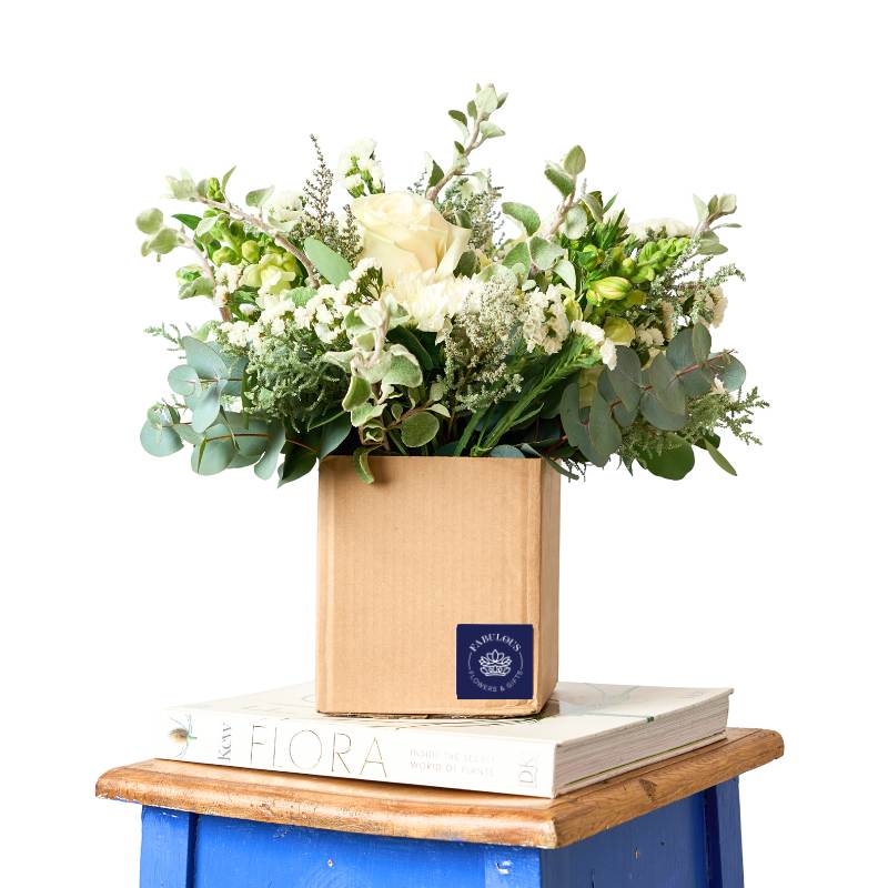 Floral arrangement in a wooden box on top of books with a visible brand logo.