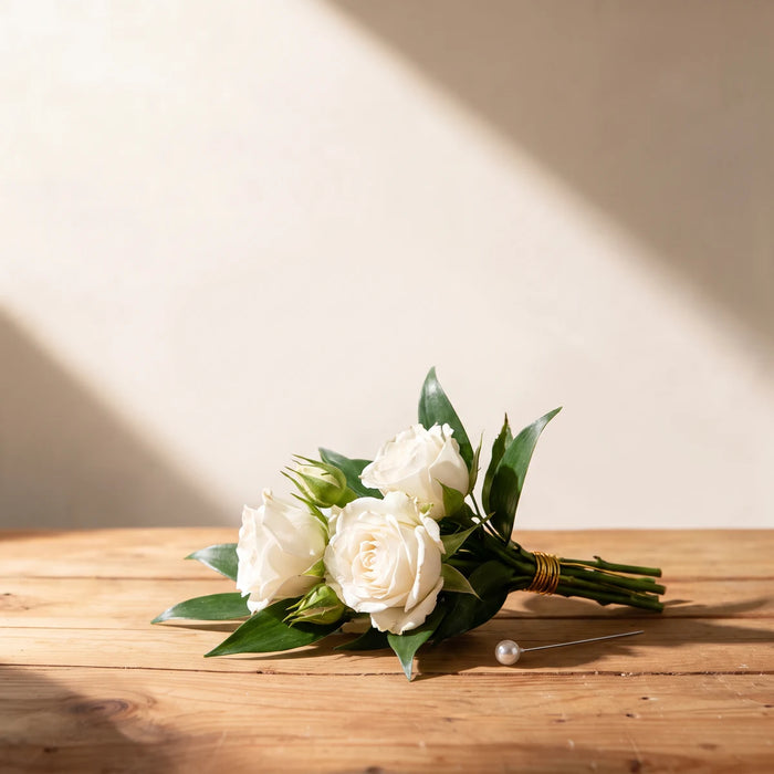 Small white spray roses and buds with dark ruscus leaves, stems bound in gold wire, lying on a pine table with a pearl pin, Fabulous Flowers South Africa