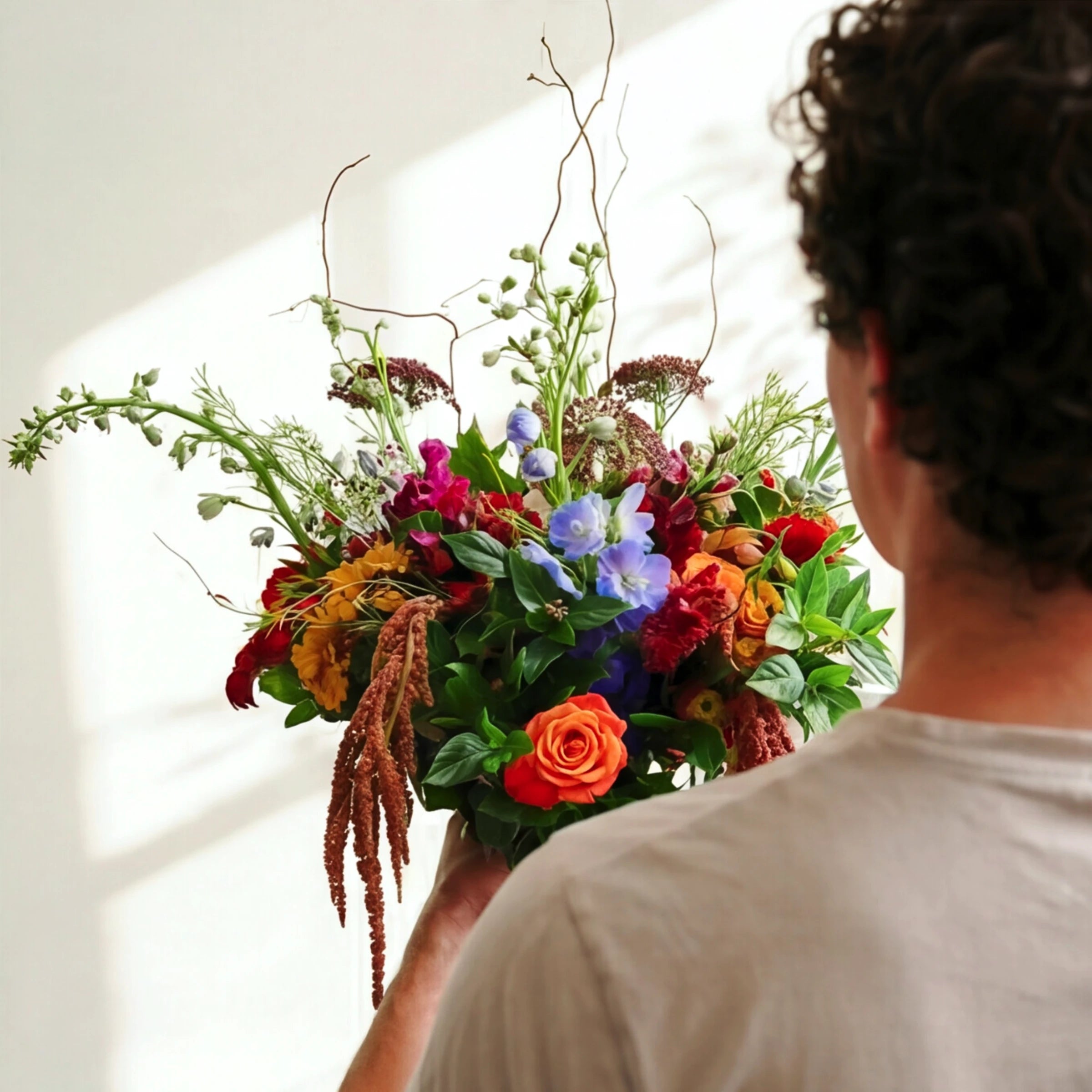 The Wild & Free wildflower bouquet over the shoulder, orange roses, blue delphinium and rust amaranthus
