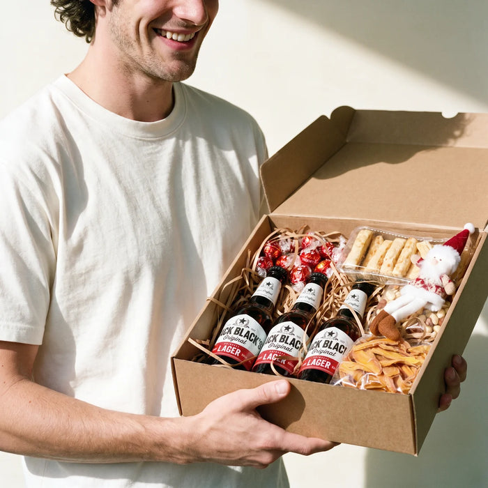 Grinning man in a white t-shirt holding an open Christmas gift box of Jack Black's lager, chocolates and snacks, Fabulous Flowers South Africa