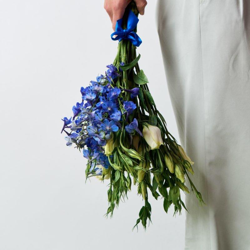 Bouquet of blue flowers held by a person wearing a white coat against a light background