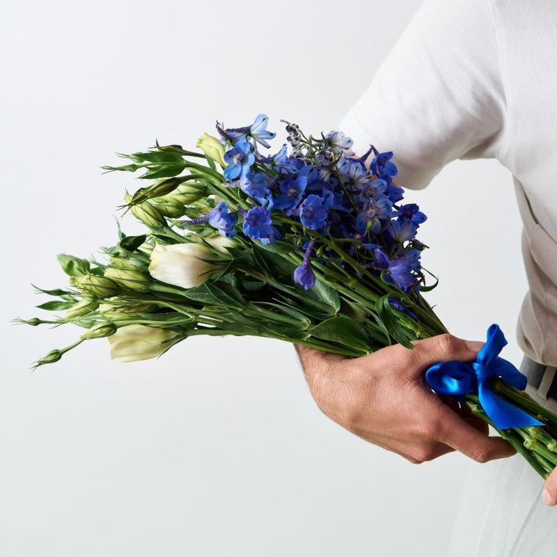 Person holding a bouquet of blue and white flowers with a plain background