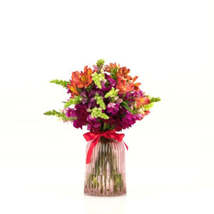 Fresh Flower arrangement in pale red glass vasewith snapdragons and alstroemeria and red ribbon