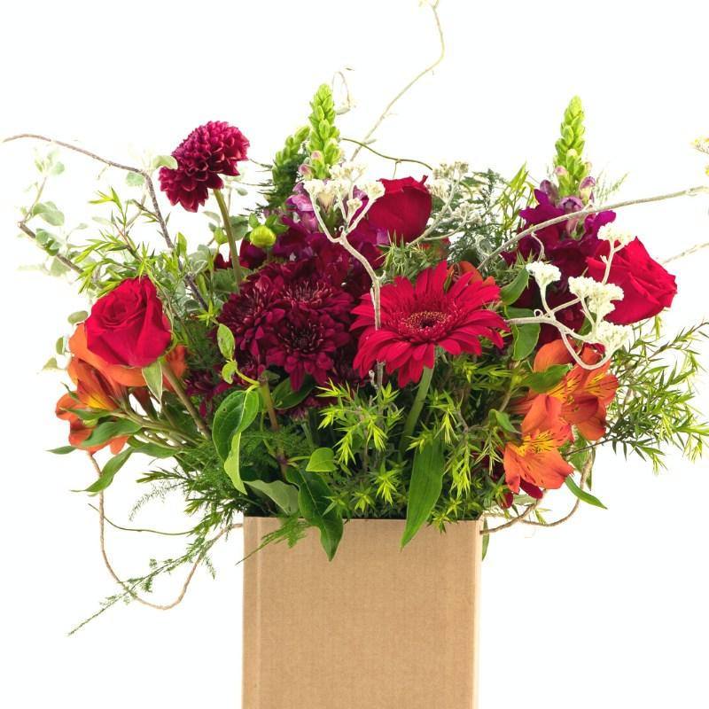 Close up of red and orange flowers like gerberas, roses, alstroemeria and greenery in a cardboard box - Fabulous Flowers